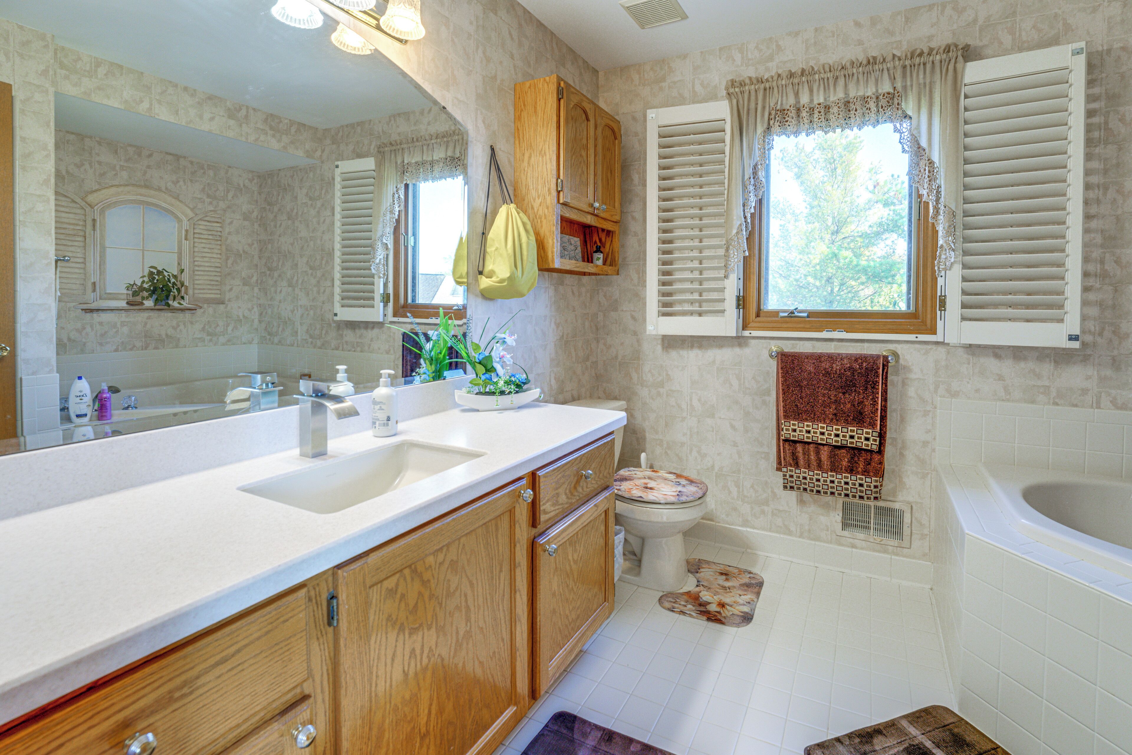 A bathroom with a large mirror, wooden cabinets, a sink, a toilet, and a bathtub.
