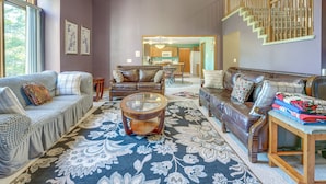 A spacious living room with a large window, a dining area, and a staircase leading to an upper floor. - Macomb Retreat w/ Spacious Yard & Fire Pit (Macomb)
