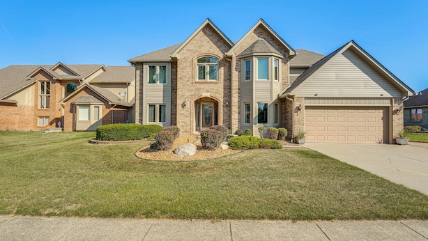 A two-story house with a garage, a well-maintained lawn, and a brick exterior. - Macomb Retreat w/ Spacious Yard & Fire Pit (Macomb)