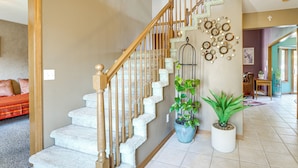 A staircase with a wooden handrail, white steps, and decorative wall art. There are potted plants on the landing. - Macomb Retreat w/ Spacious Yard & Fire Pit (Macomb)
