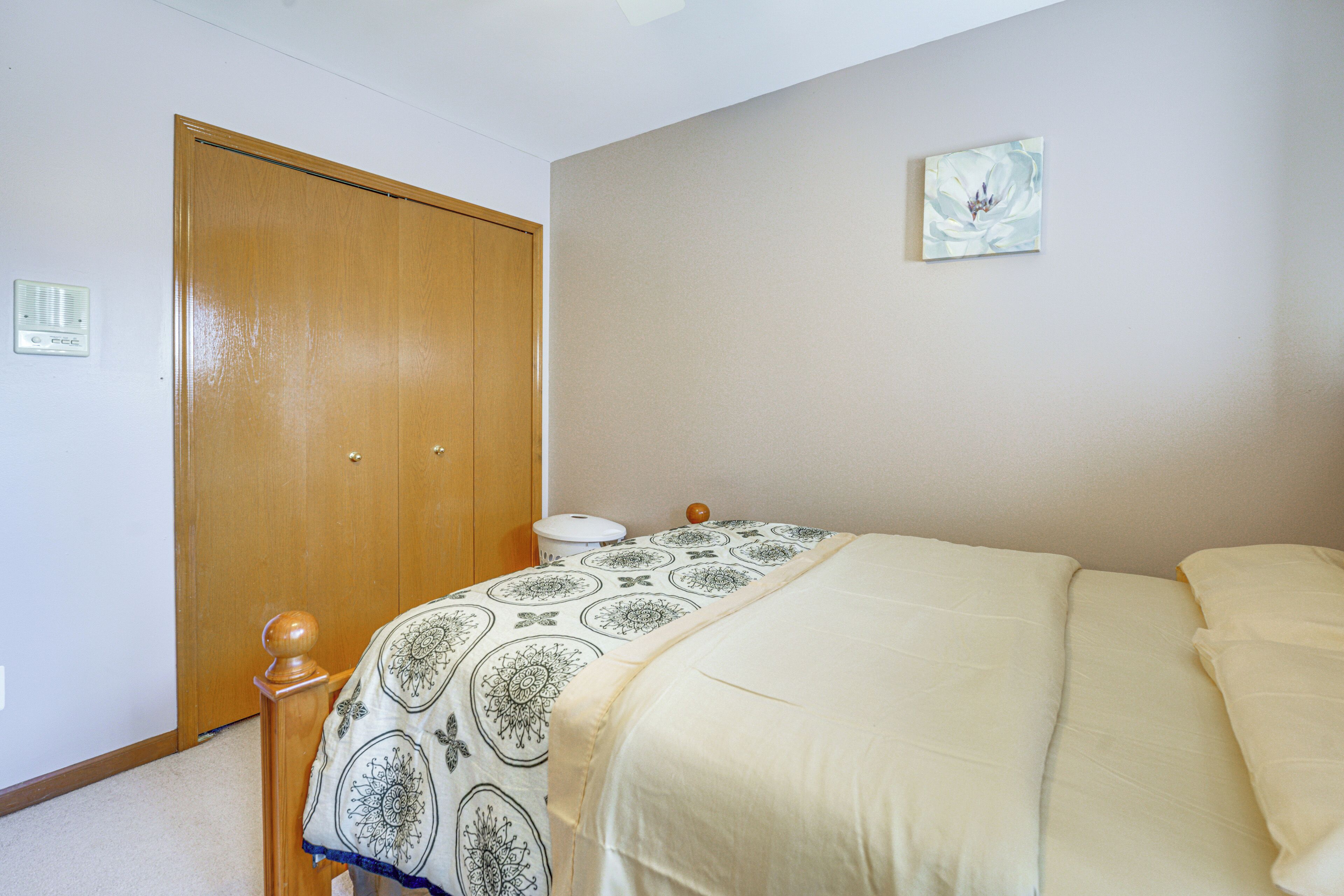 Een slaapkamer met een houten deur, een nachtkastje met een lamp, een bed met een beddengoed met patroon, en een aan de muur hangend schilderij.