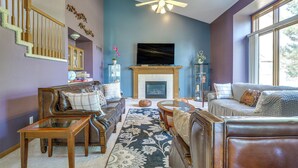 A living room with a fireplace, a sofa, a coffee table, and a television. - Macomb Retreat w/ Spacious Yard & Fire Pit (Macomb)
