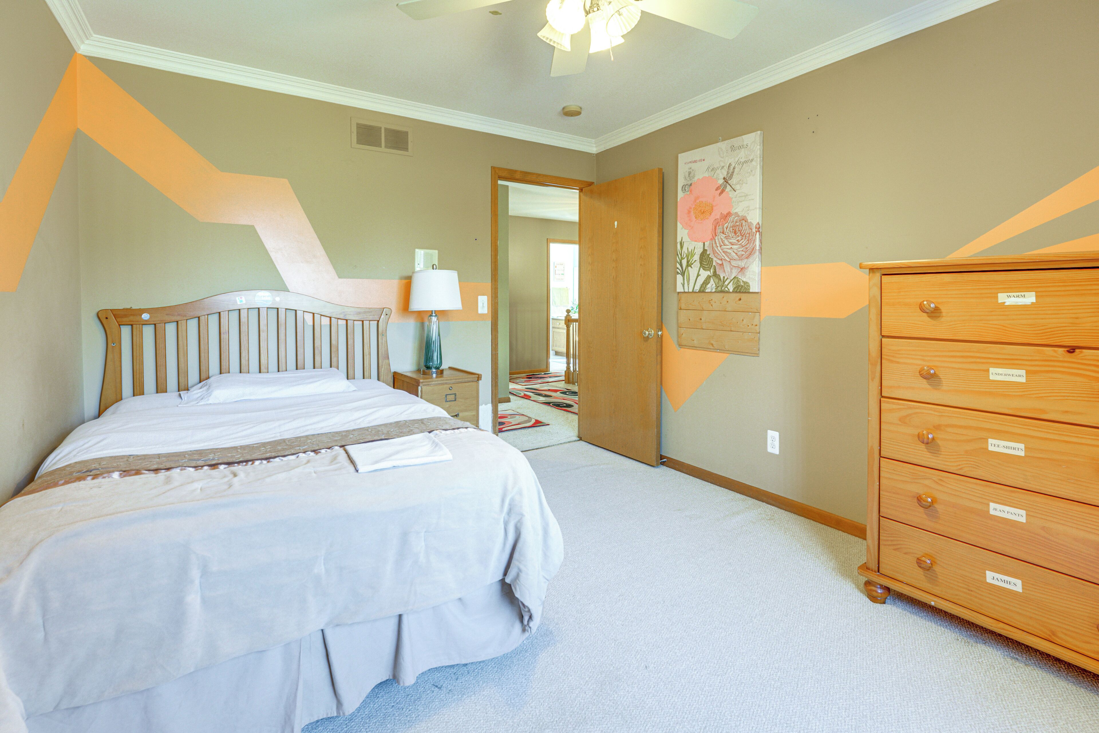 A bedroom with a bed, a dresser, and a door leading to another room.