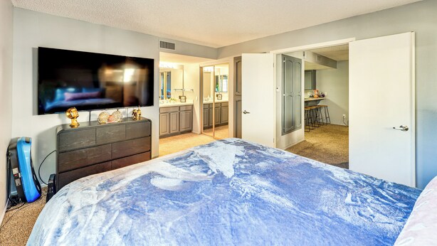 Een slaapkamer met een bed, een dressoir, een televisie en een badkamer die door een open deur zichtbaar is.