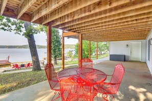 Un espacio al aire libre techado, con techo de madera, una mesa redonda de metal rojo y sillas, y vistas a un lago.