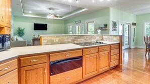 A spacious kitchen with wooden cabinets, a large island, and a flat-screen TV. - Water-view Deck! Family Home on Lake of the Ozarks (Roach)