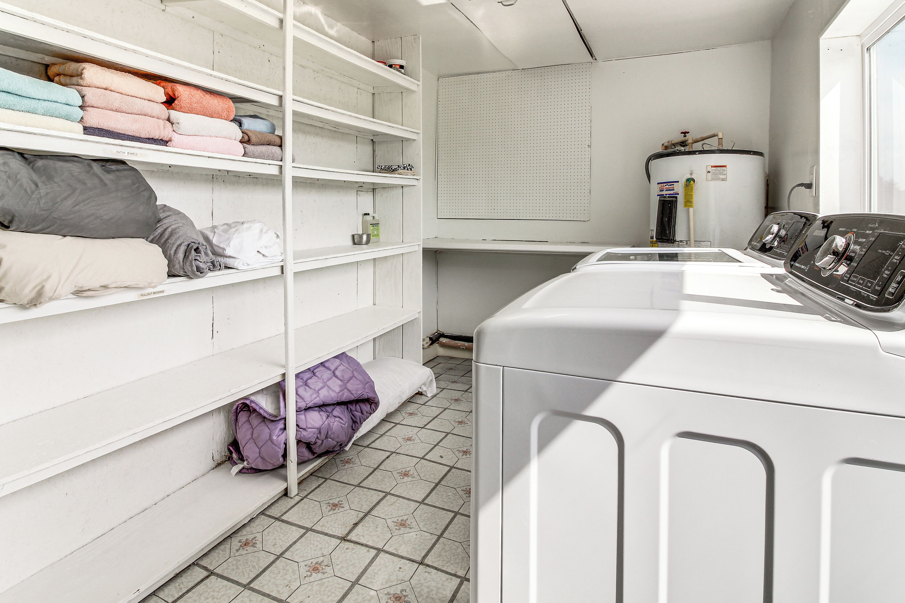 A laundry room with shelves of folded clothes, a water heater, and a washing machine.
