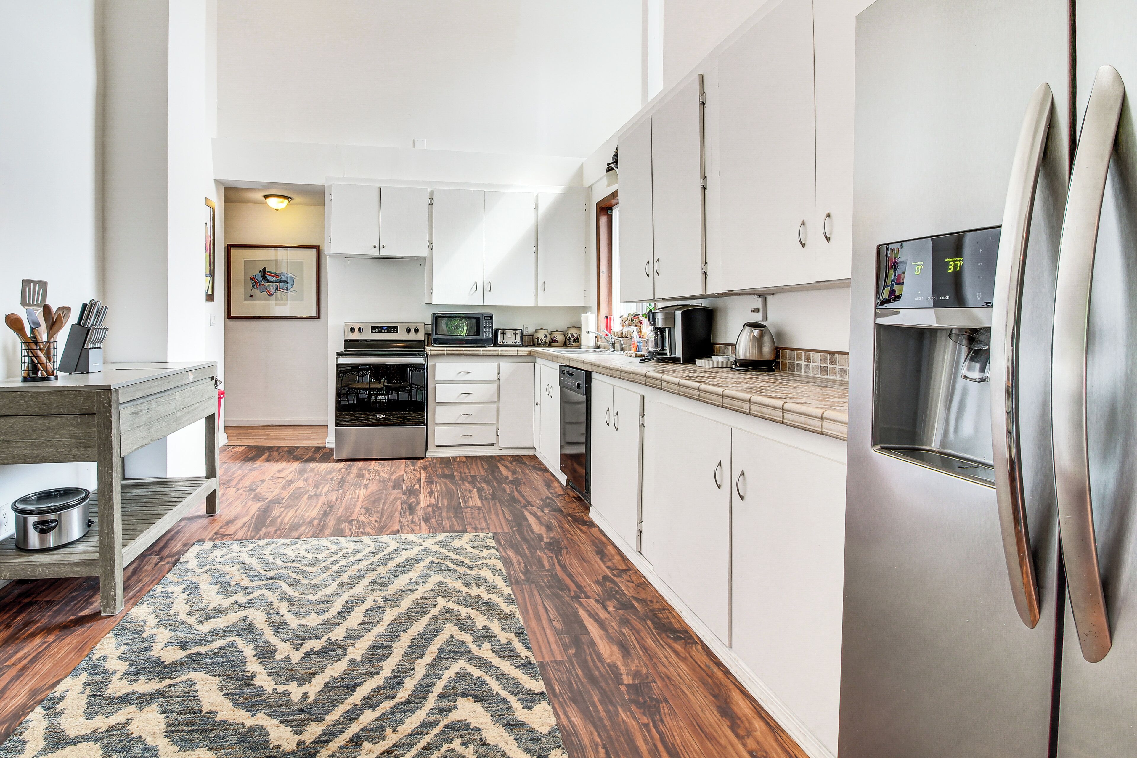 A modern kitchen with white cabinets, stainless steel appliances, and a wooden floor.