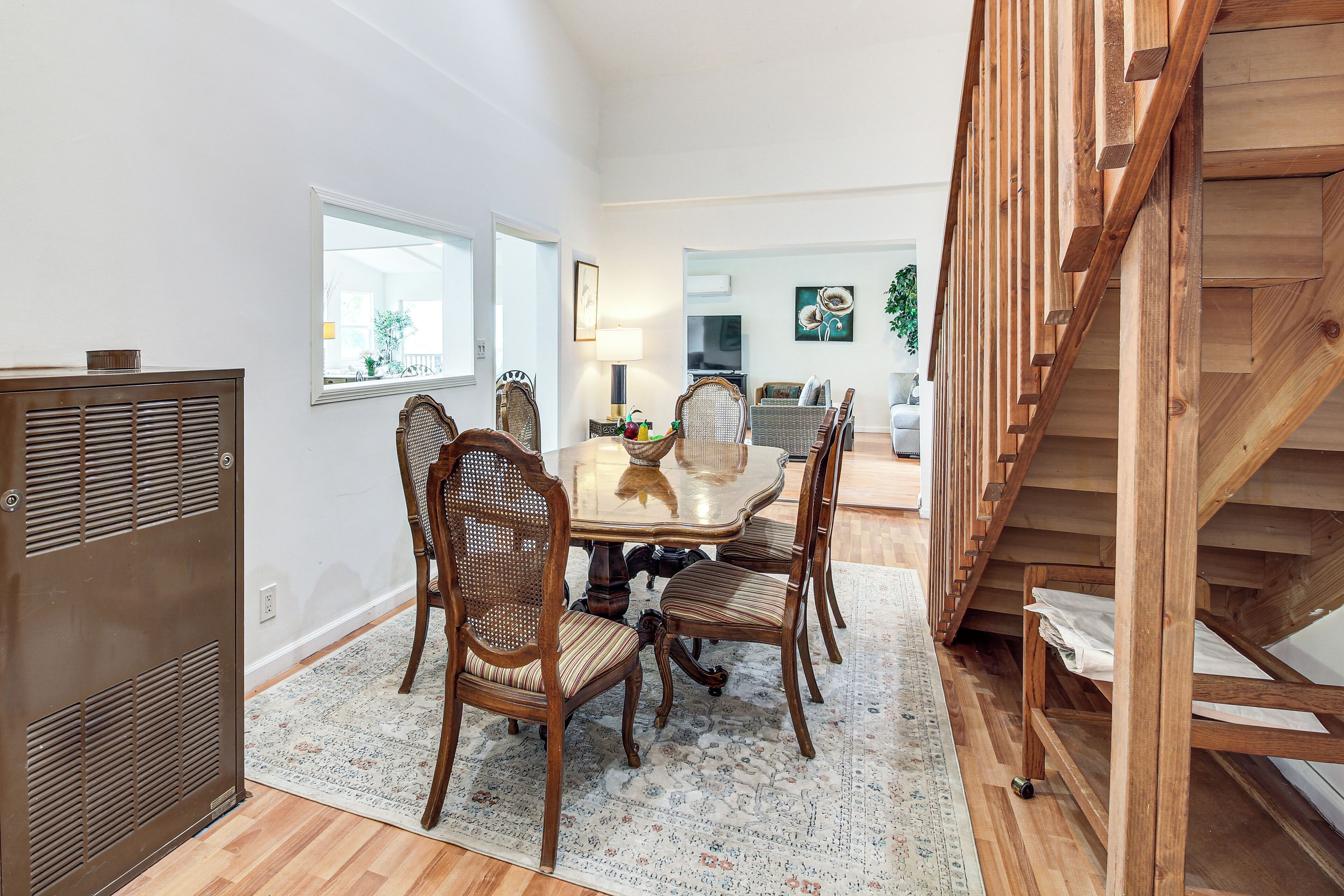 A dining area with a wooden table and chairs, a patterned rug, and a staircase to the right.