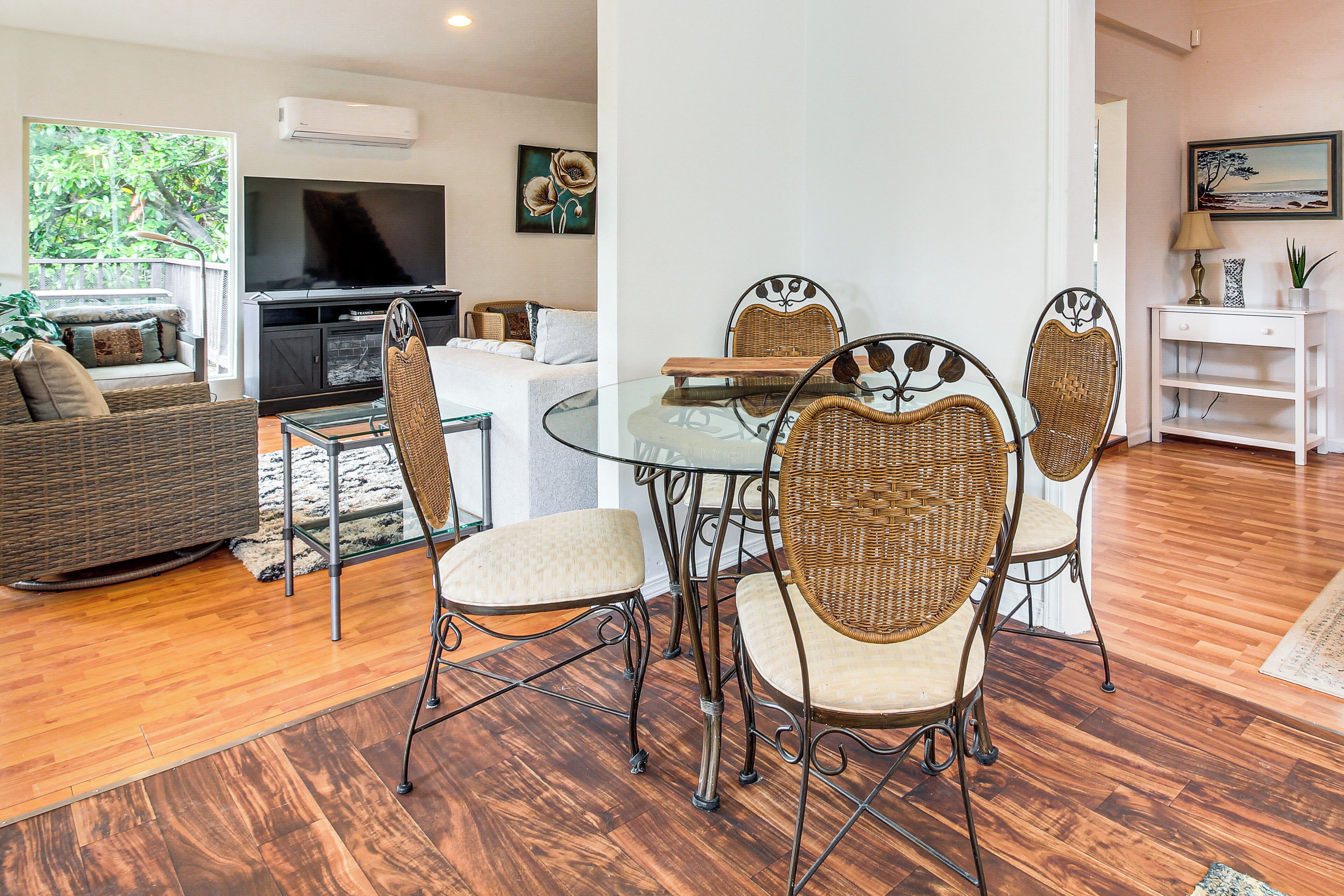A living room with a glass-top dining table surrounded by wicker chairs, a sofa, and a television.