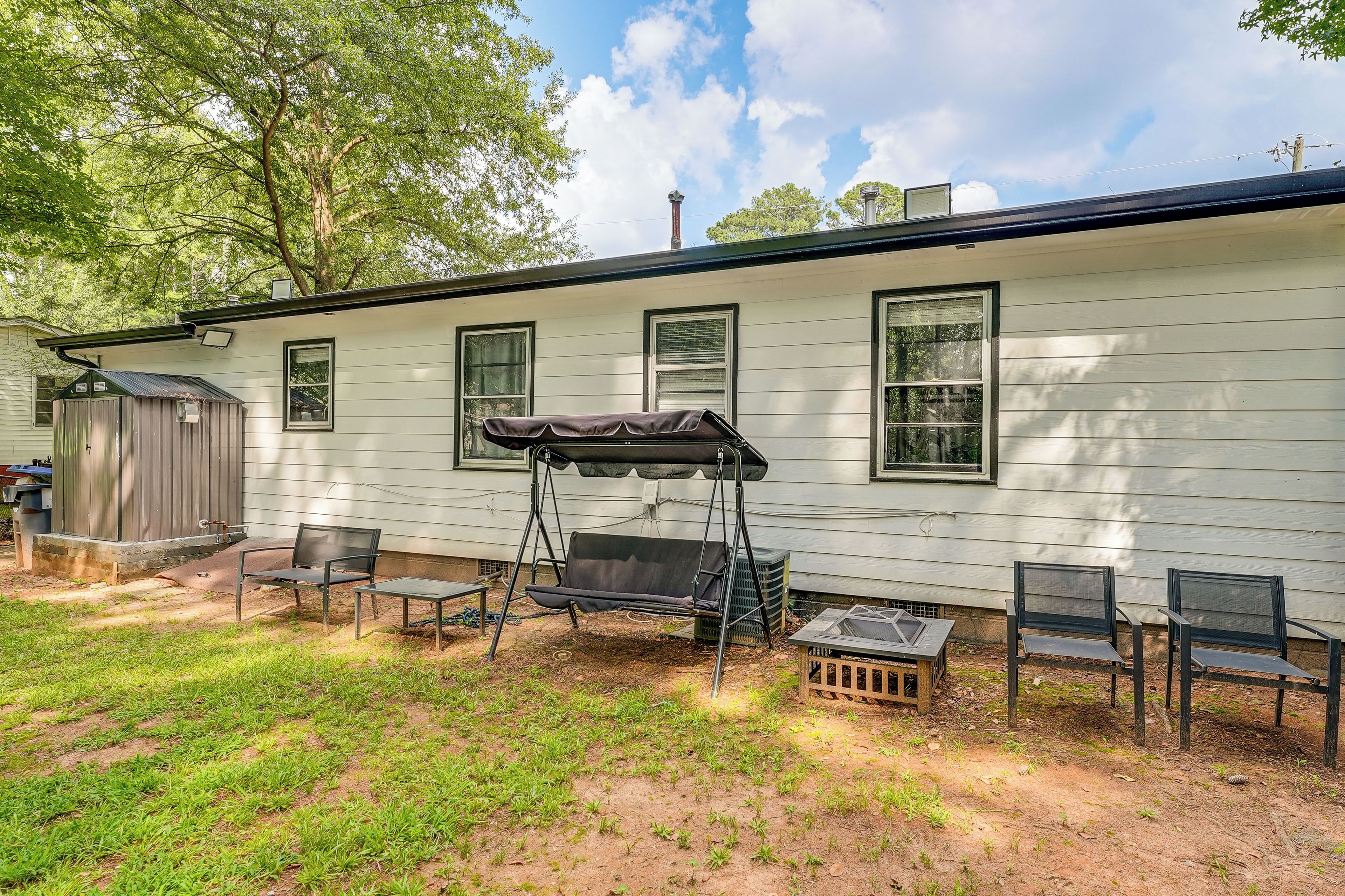 A single-story house with a covered outdoor seating area, a small shed, and a grassy yard.