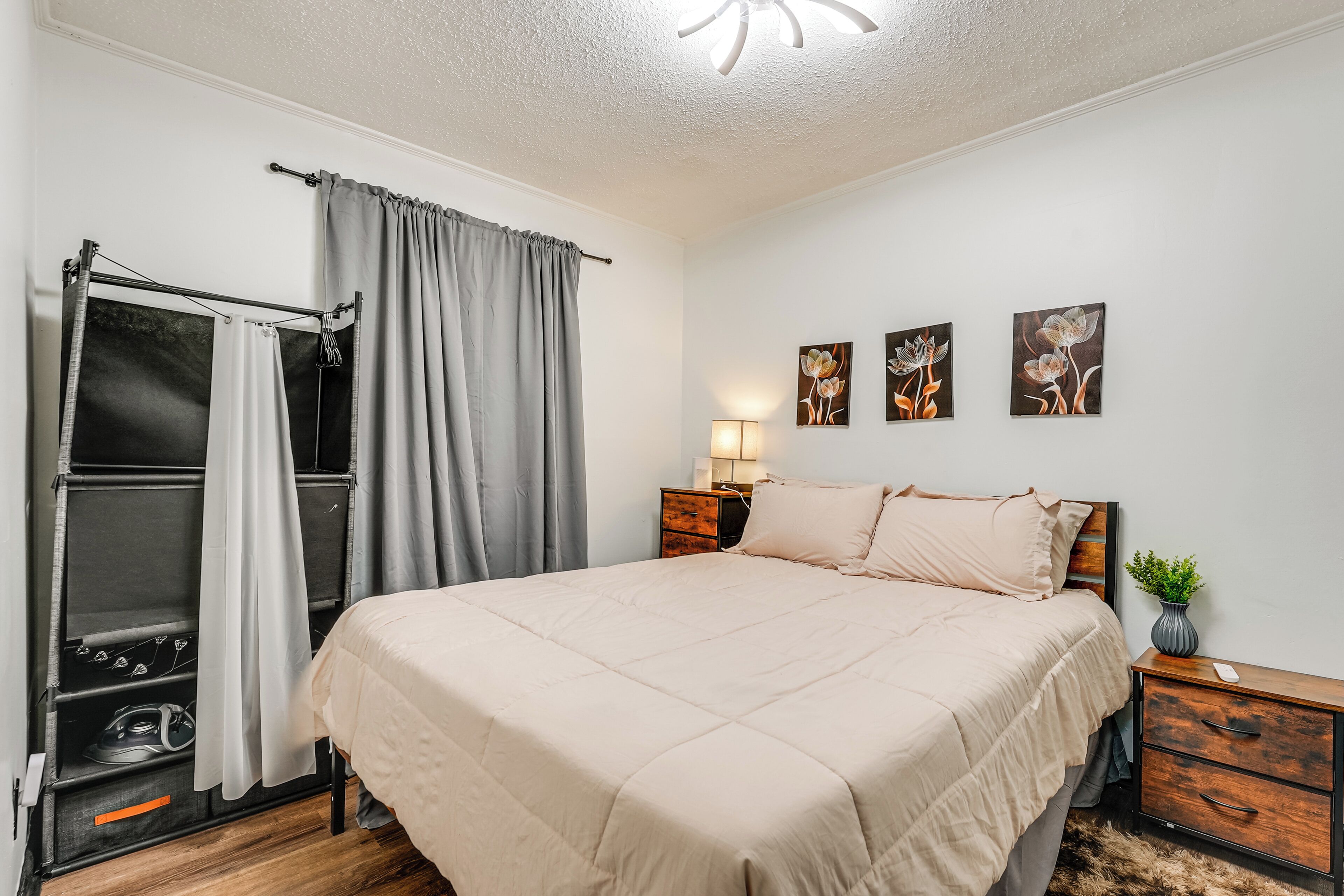 Ein Schlafzimmer mit einem Bett, einem Nachttisch, einer Lampe und einer Wand mit drei floralen Bildern.