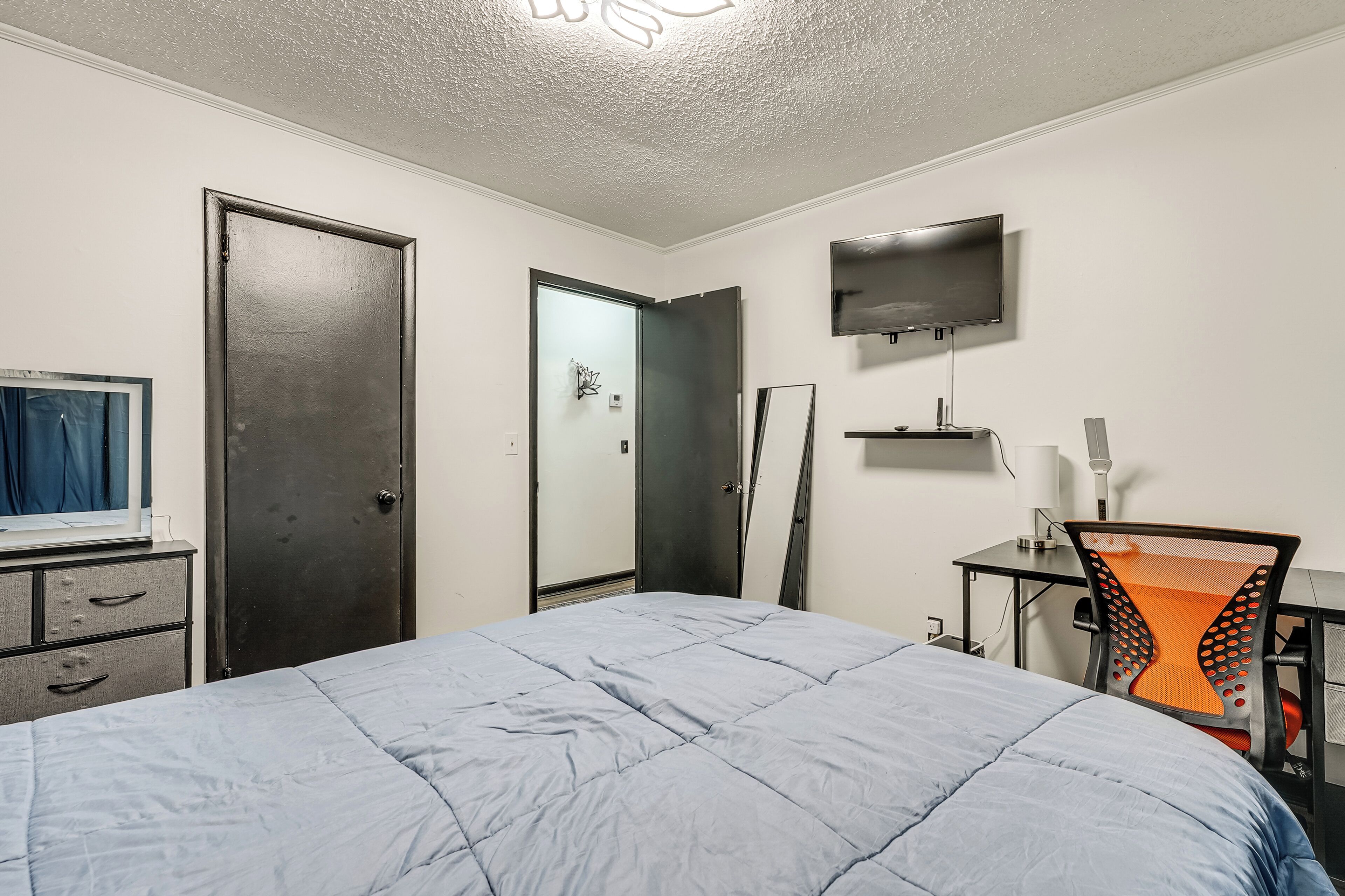 A bedroom with a bed, a desk, a chair, a TV, and a wardrobe.