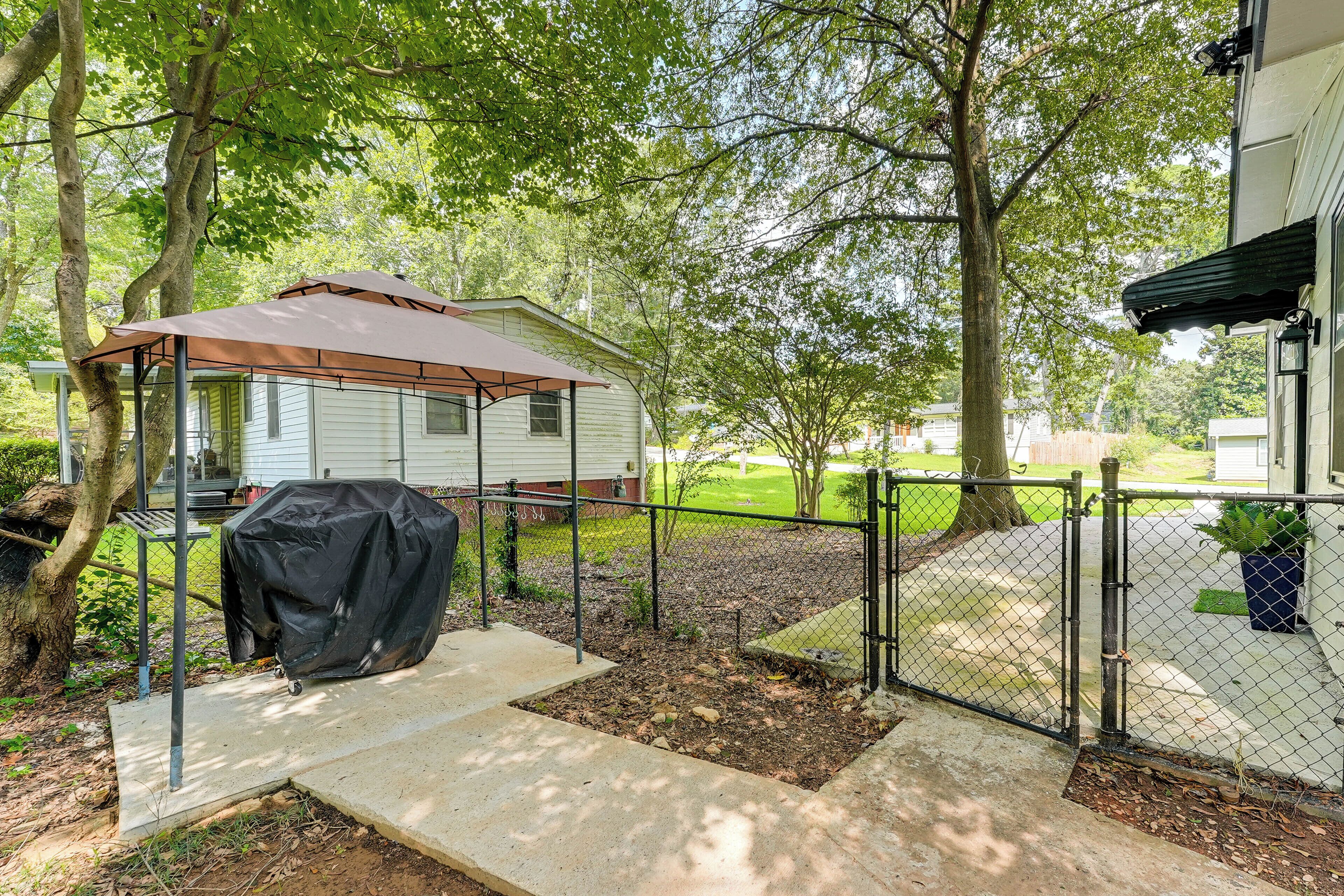 Un patio couvert avec un barbecue, une cour clôturée et une maison en arrière-plan.