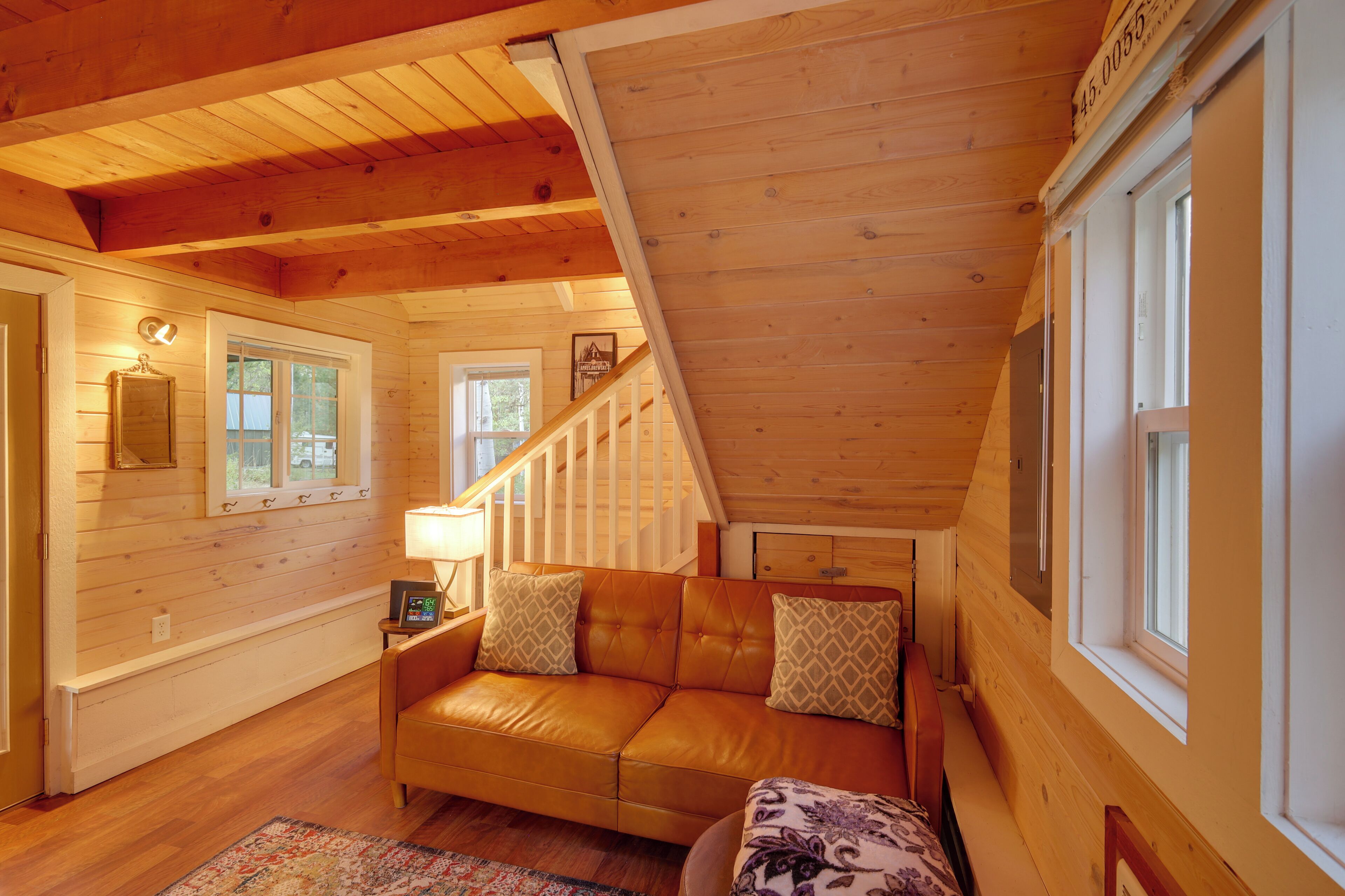 A cozy wooden cabin interior with a leather sofa, a patterned rug, and a staircase leading to an upper level.