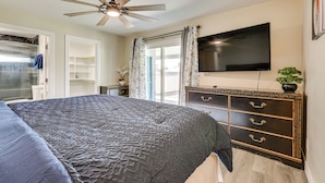 Une chambre à coucher avec un lit, un ventilateur de plafond, une commode, un téléviseur et une fenêtre avec des rideaux.