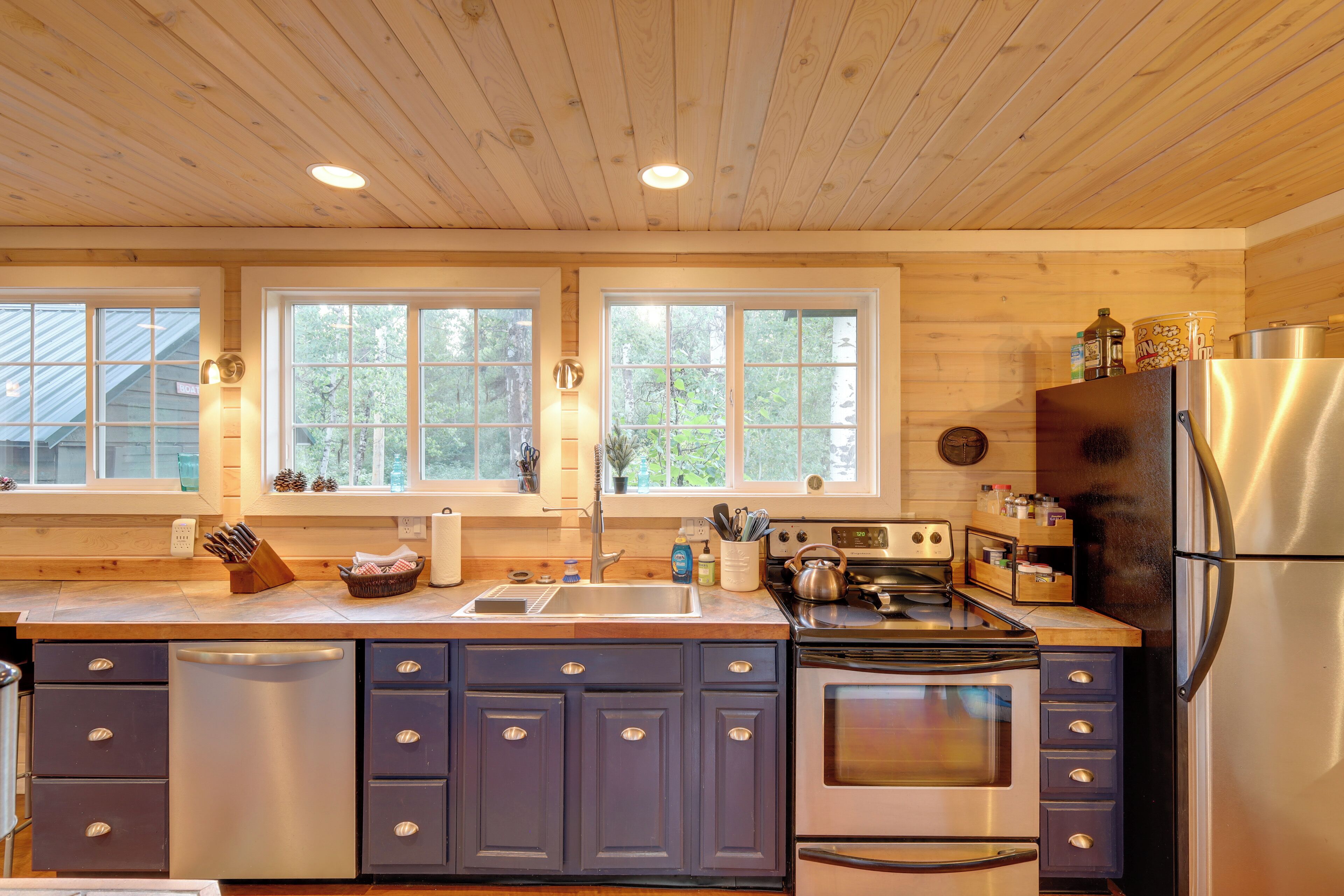 A modern kitchen with wooden cabinets, stainless steel appliances, and large windows.