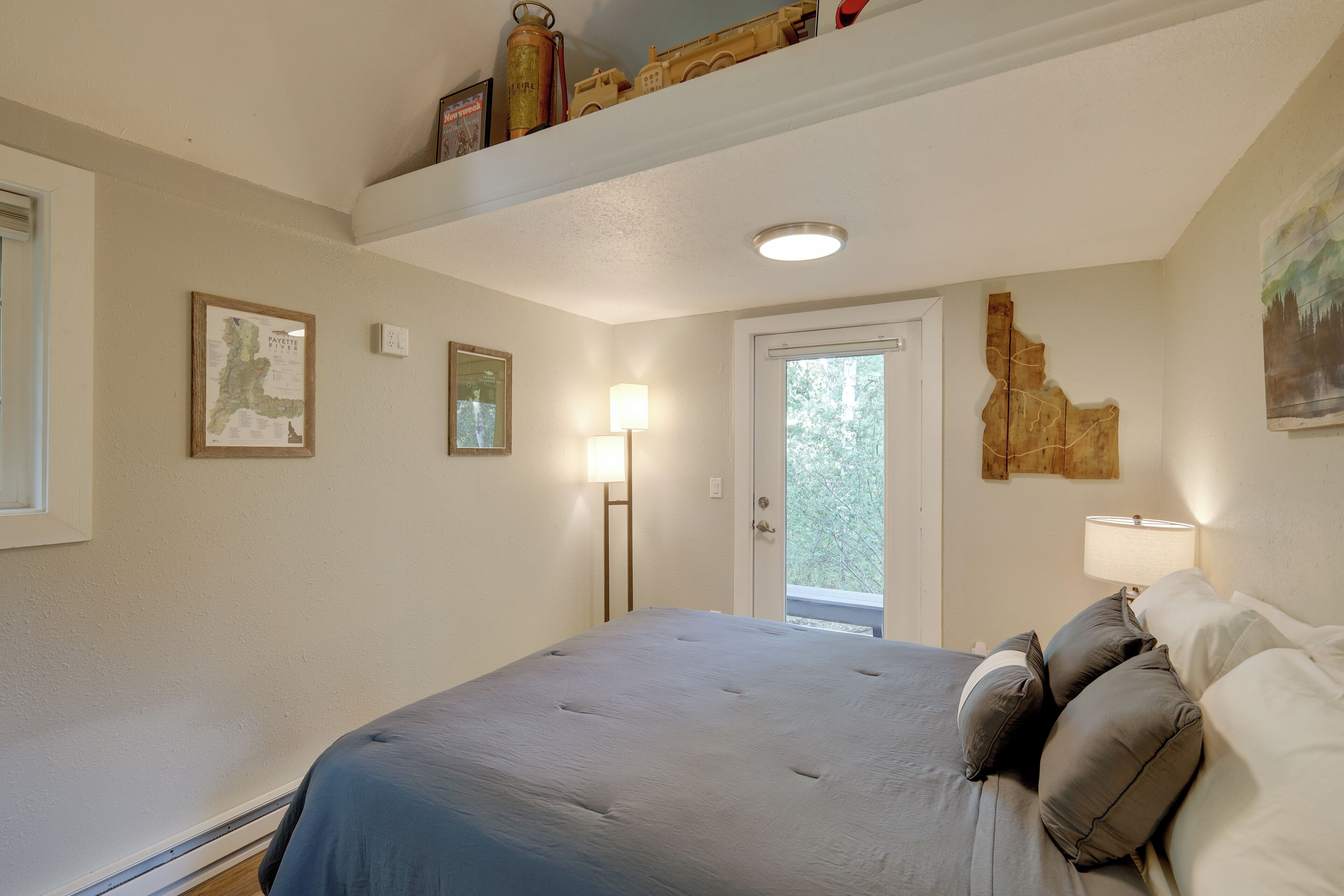 Quarto com cama, porta, janela e obras de arte na parede.
