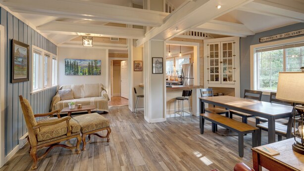 Amplia sala de estar con piso de madera, un sofá, una mesa de comedor con sillas y una cocina con armarios y una ventana.