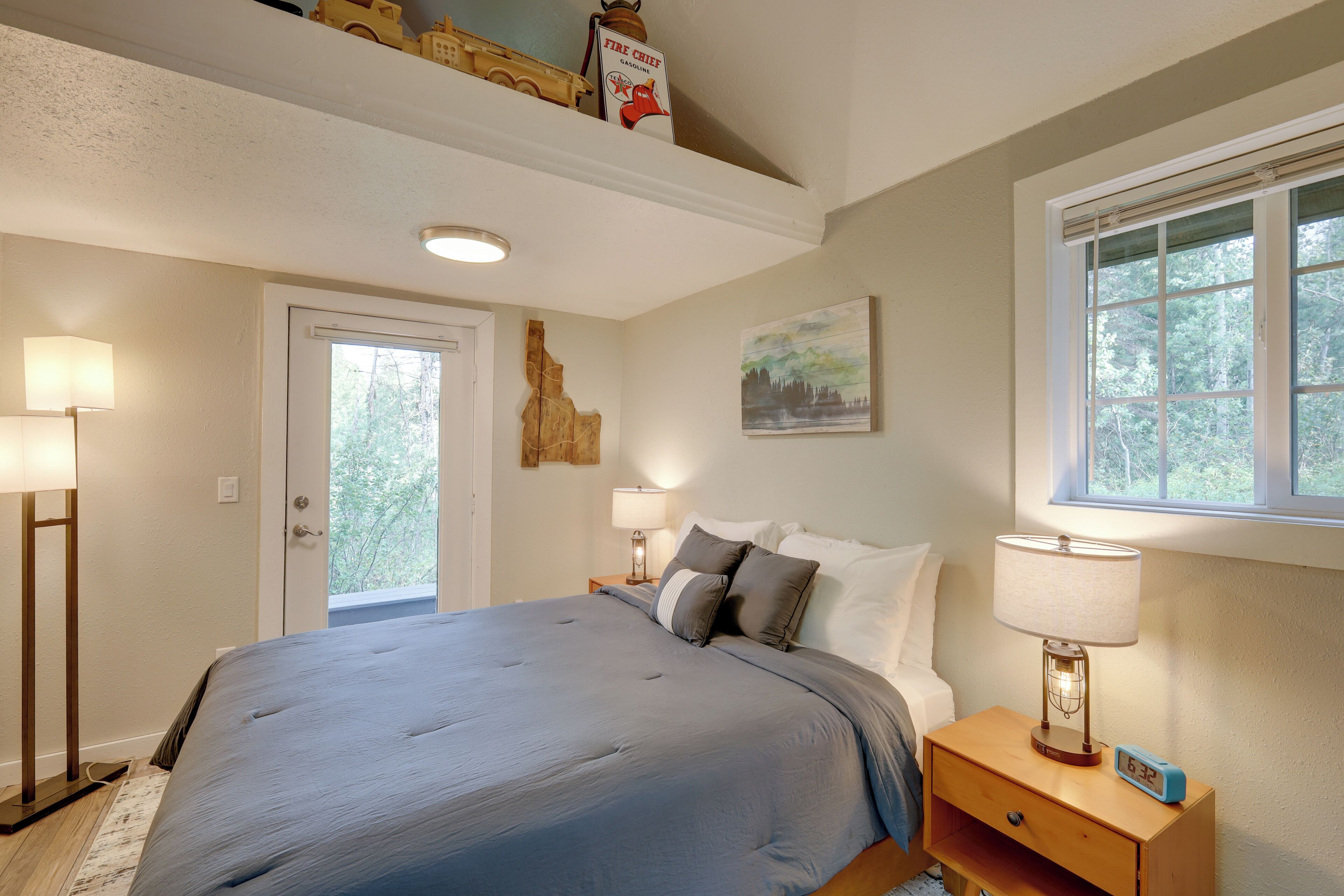 A bedroom with a large bed, bedside lamps, a nightstand, a window with a view of trees, and a ceiling light.
