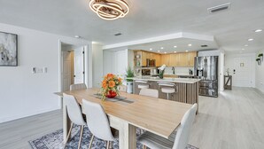 A modern kitchen with stainless steel appliances, a wooden dining table with chairs, and a central island. - Sunset Views & Hot Tub: Lakefront Holiday Retreat! (Holiday)
