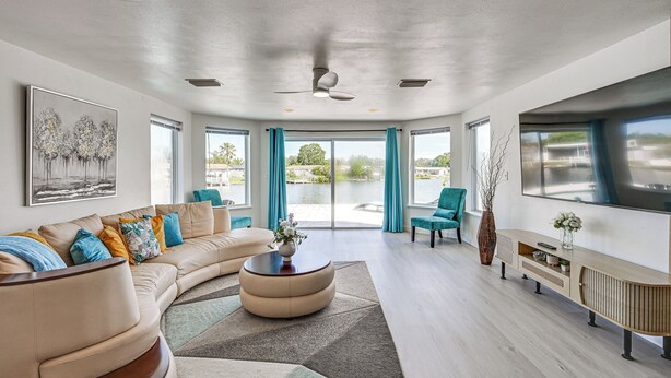 A modern living room with a curved sofa, a round coffee table, and a TV on a wooden console. - Sunset Views & Hot Tub: Lakefront Holiday Retreat! (Holiday)
