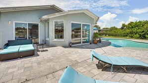 A modern house with a patio area featuring a pool, a built-in sofa, and two lounge chairs. - Sunset Views & Hot Tub: Lakefront Holiday Retreat! (Holiday)