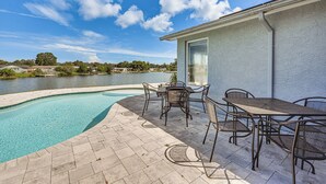 A swimming pool with a patio area, outdoor furniture, and a view of a lake. - Sunset Views & Hot Tub: Lakefront Holiday Retreat! (Holiday)