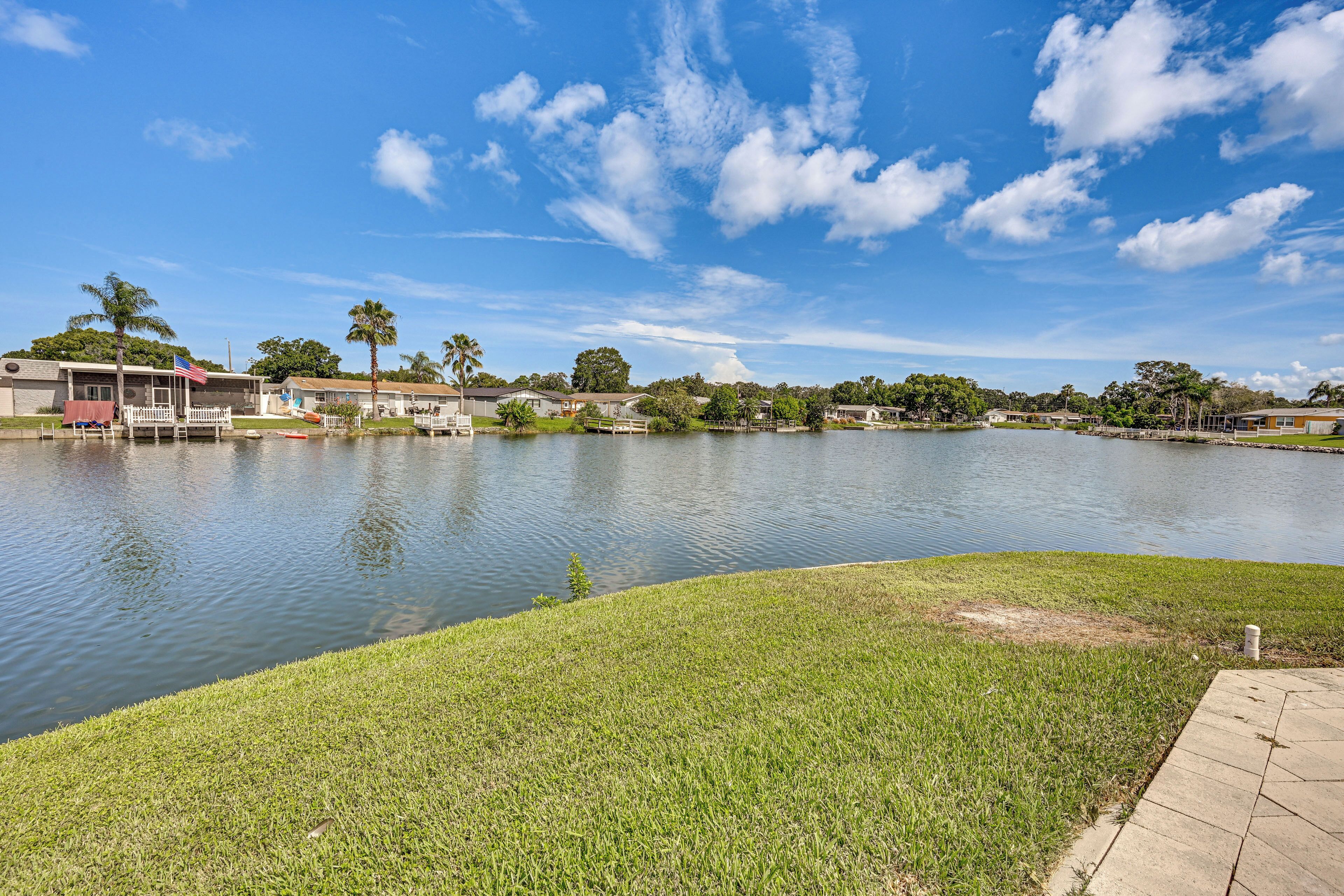 Vista de un lago con una zona verde, un muelle y edificios al fondo.
