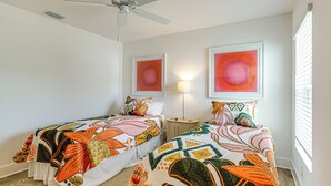 Un dormitorio con dos camas, cada una con una colcha de colores, un ventilador de techo y obras de arte en las paredes.