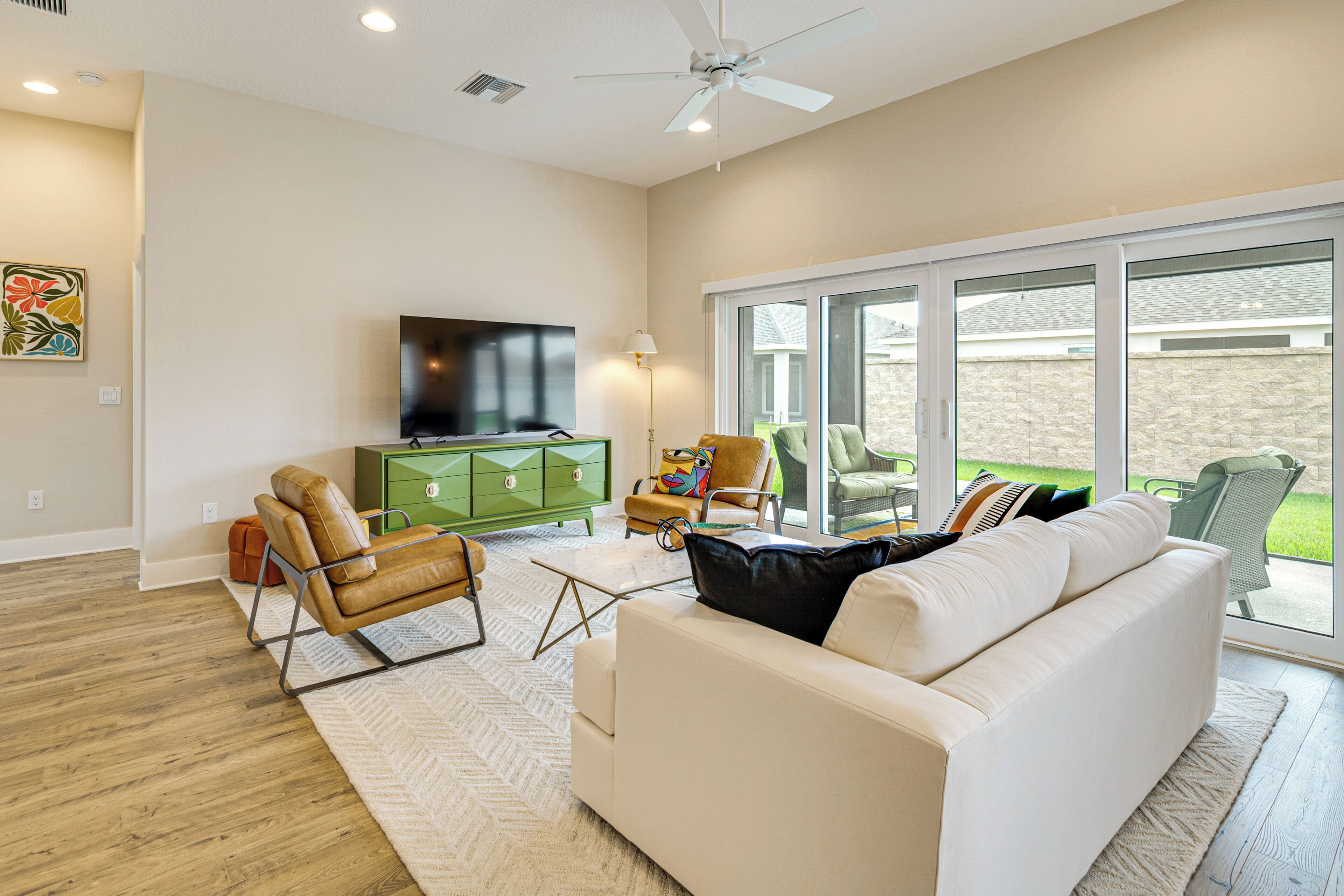 A modern living room with a white sofa, a green cabinet, a leather armchair, and a flat-screen TV.