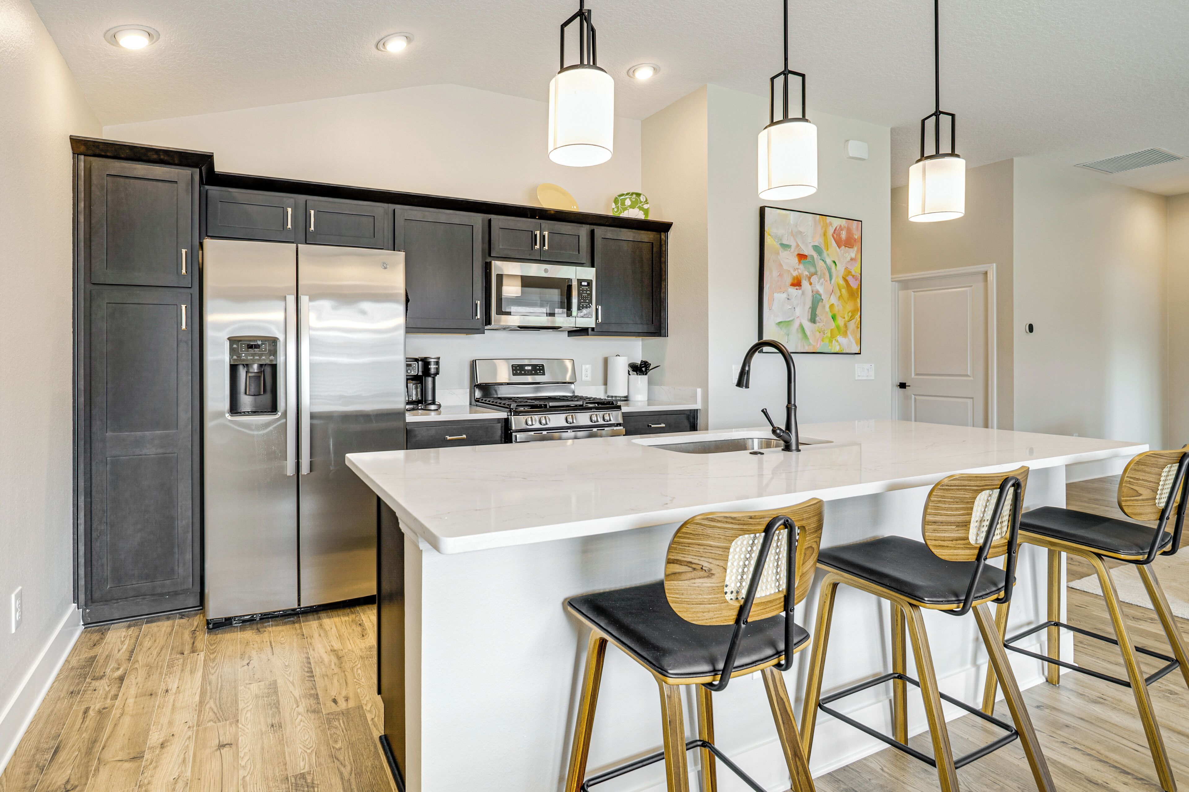 A modern kitchen with dark cabinets, stainless steel appliances, a large island, and bar stools.