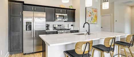 A modern kitchen with dark cabinets, stainless steel appliances, a large island, and bar stools.