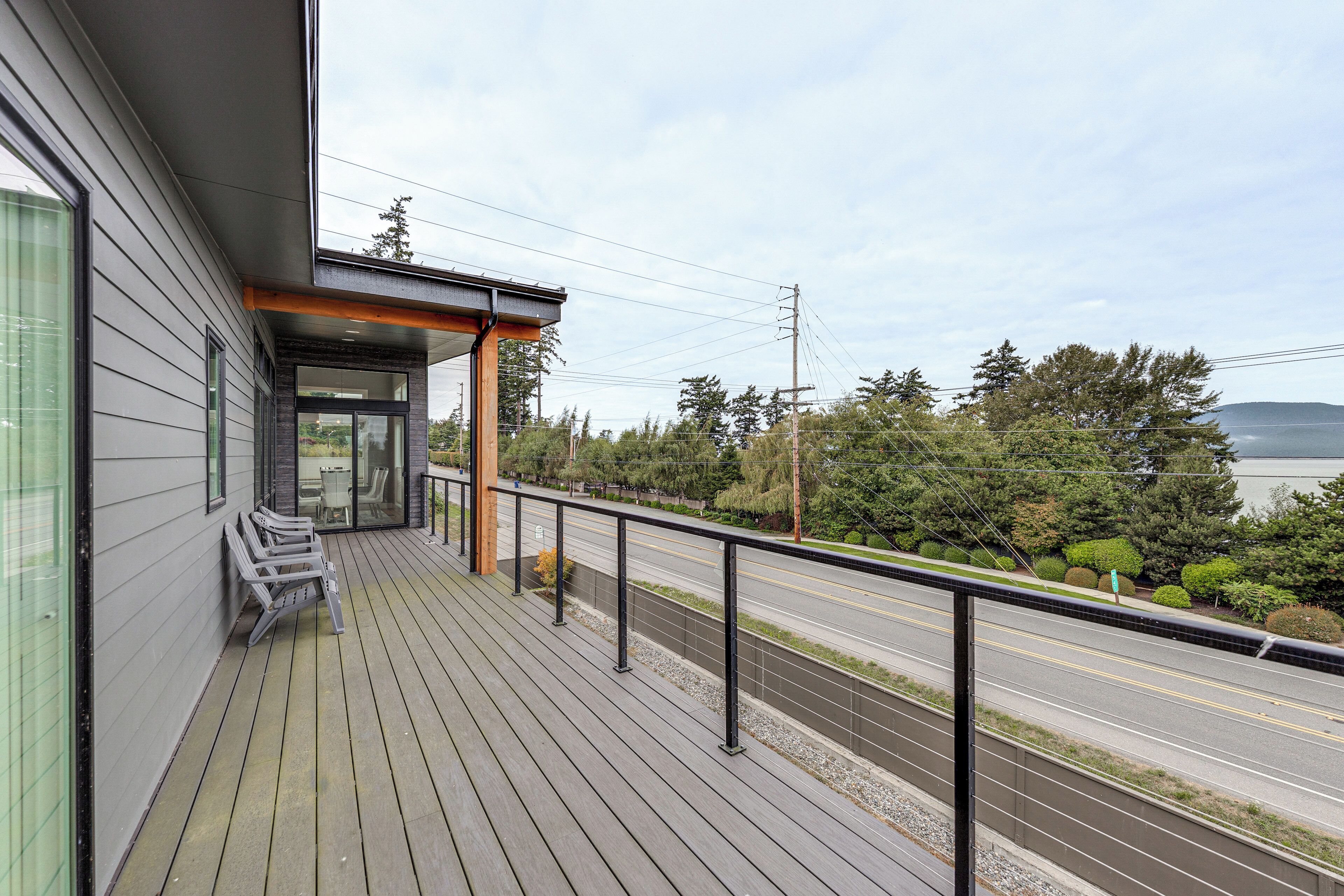 Een modern gebouw met een houten terras, zitplaatsen buiten en uitzicht op een weg en groen.