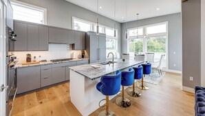 A modern kitchen with grey cabinets, a marble island, and blue bar stools. - Fenced Yard, Water & Island Views: Anacortes Home! (Anacortes)