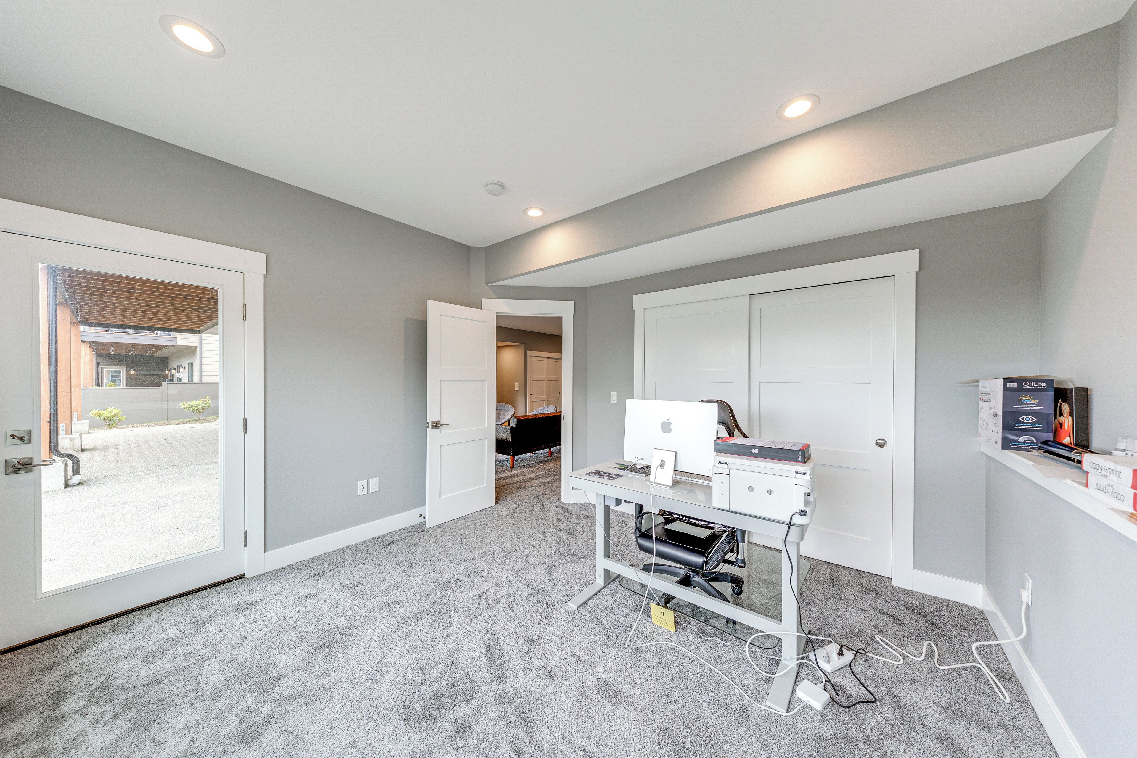 Een moderne kamer met een bureau, computer en printer, vloerbedekt met tapijt, en een deur die naar een andere kamer leidt.