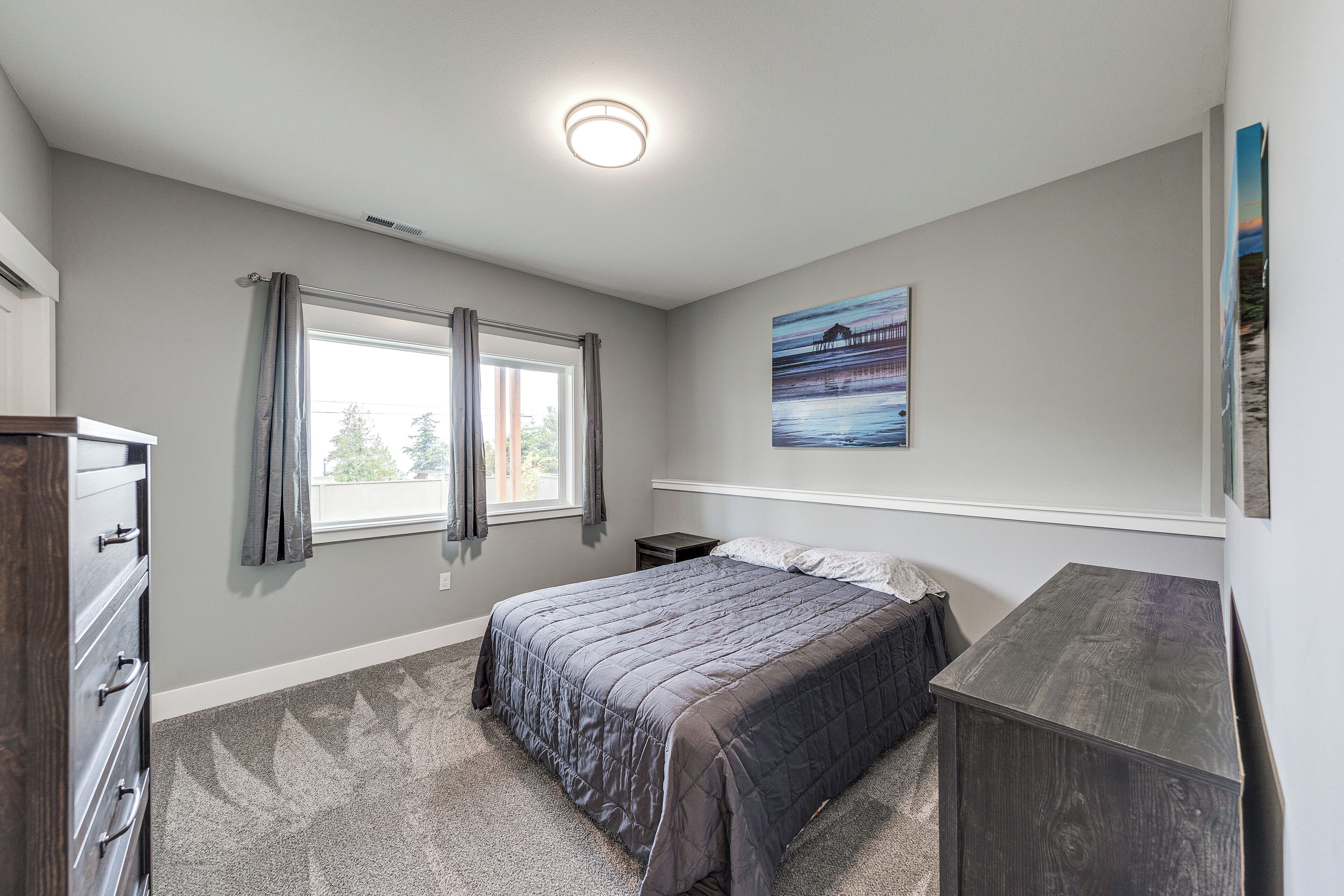 A bedroom with a bed, dresser, window with curtains, and a painting on the wall.