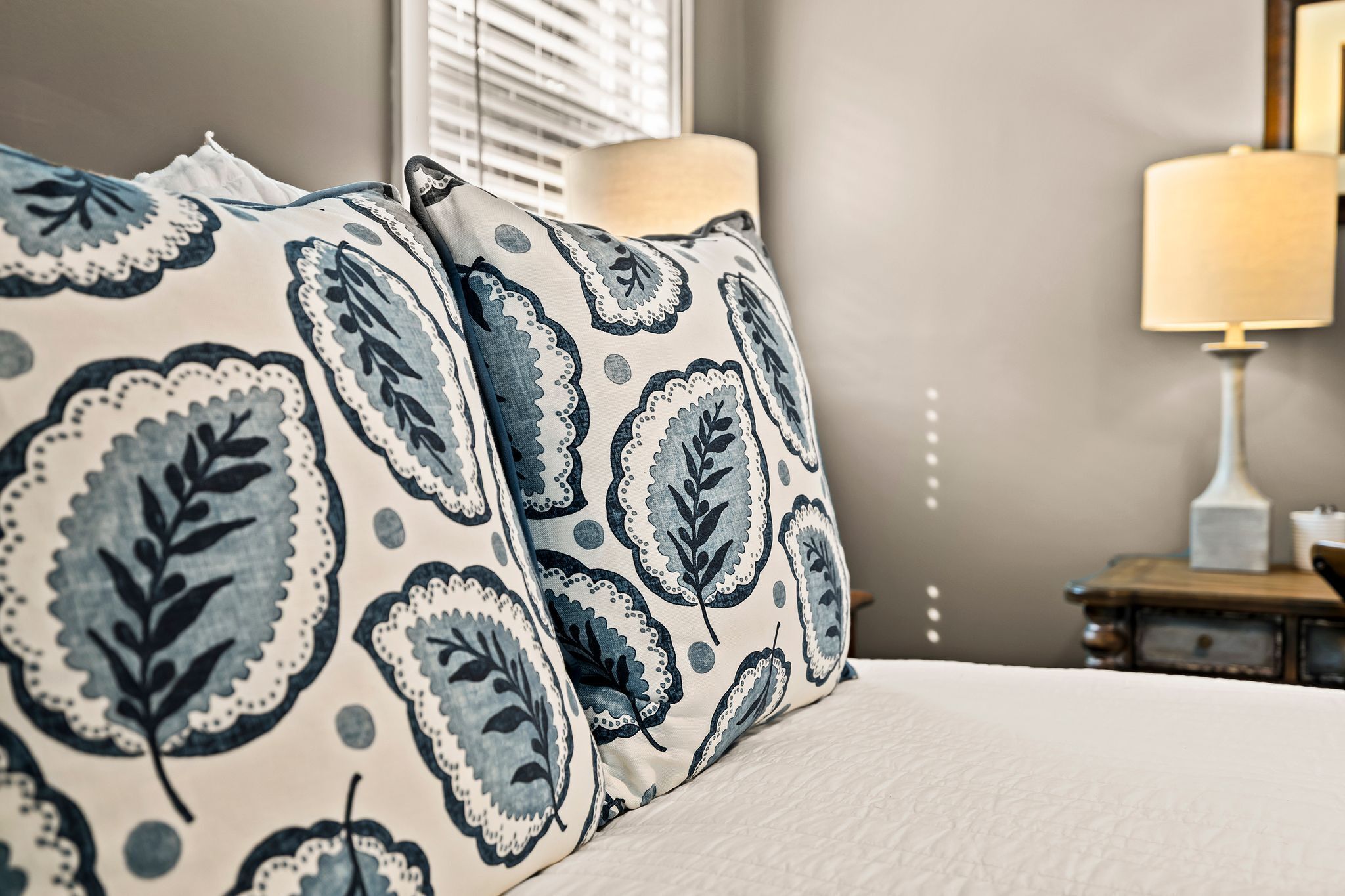 A bed with a patterned pillow, a bedside lamp, and a nightstand with a lamp.
