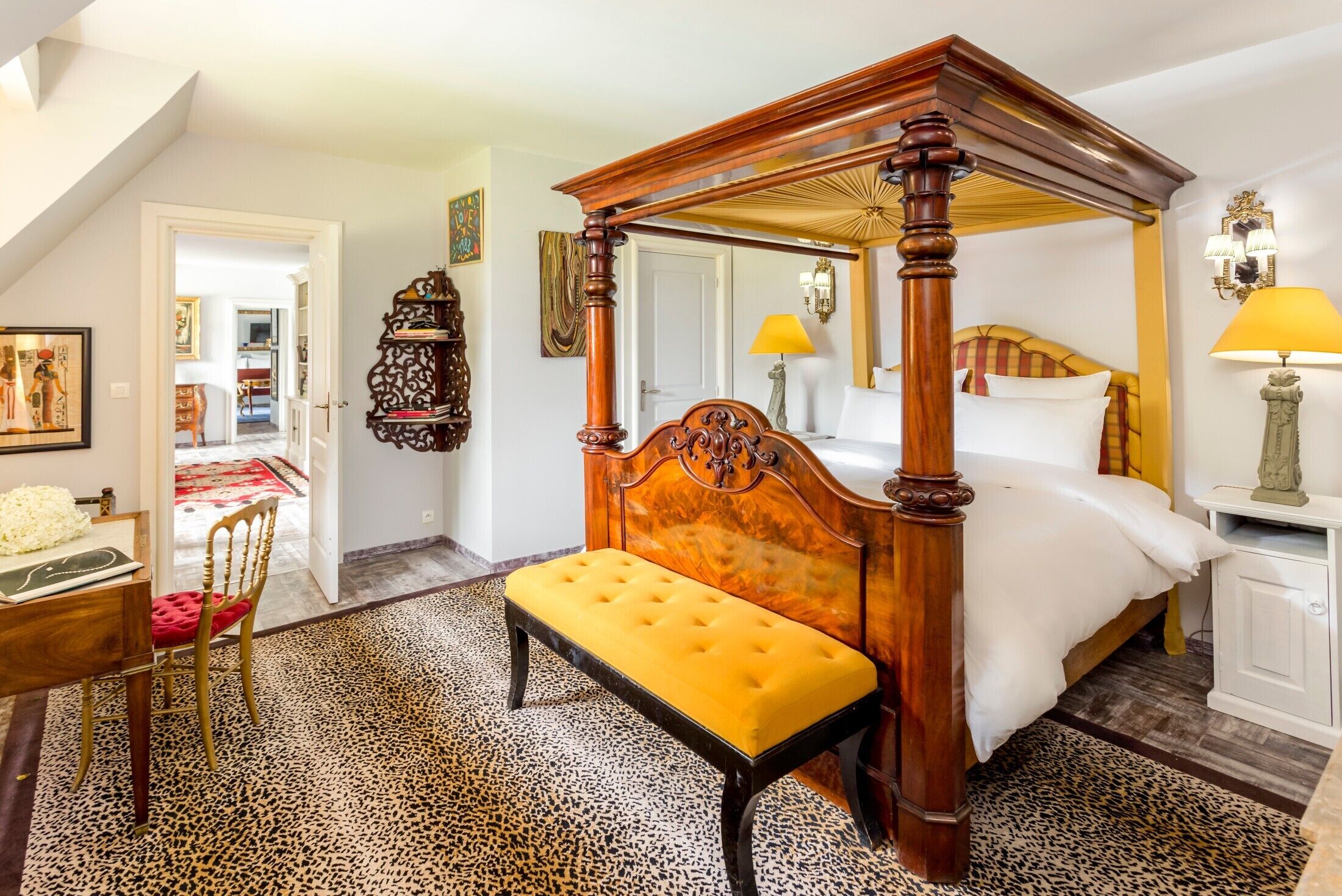A four-poster bed with a bench, a desk with a chair, and a leopard print rug.