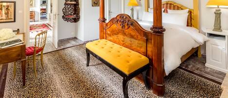 A four-poster bed with a bench, a desk with a chair, and a leopard print rug.