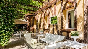 An outdoor patio with wicker furniture, a white table, and a hanging chair. - Domaine de la Boisisère (Trouville-la-Haule)