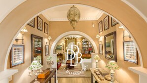 An arched hallway with a chandelier, framed pictures, and a bookshelf. - Domaine de la Boisisère (Trouville-la-Haule)