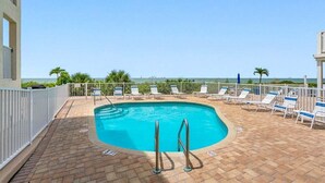 Une piscine sur le toit offrant une vue dégagée sur l’océan, entourée de chaises longues et d’une clôture blanche.