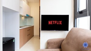 A modern living room with a flat-screen TV displaying the Netflix logo, a sofa, and a kitchen area in the background. - Studio in Modern building with AC; Kitchen; 1.3km from TSN airport (Hồ Chí Minh)