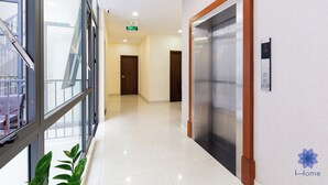 A modern hotel corridor with a glass wall, a wooden-framed elevator, and a sign indicating the direction to the exit. - Studio in Modern building with AC; Kitchen; 1.3km from TSN airport (Hồ Chí Minh)