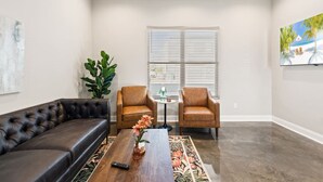 Un salón con un sofá de cuero, dos sillones de cuero, una mesa de centro con un jarrón de flores y un cuadro en la pared.