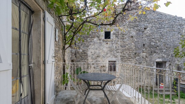 Un balcón con una mesa y sillas, un muro de piedra y un ventanal pequeño.