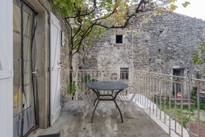 A balcony with a table and chairs, a stone wall, and a small window. - Holiday Home 'Chez L'Oncle' with Air Conditioning (Gras)