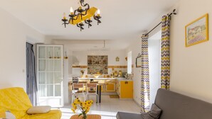 Una sala de estar con un sofá, una mesa de centro y una zona de comedor con sillas, y una cocina al fondo.