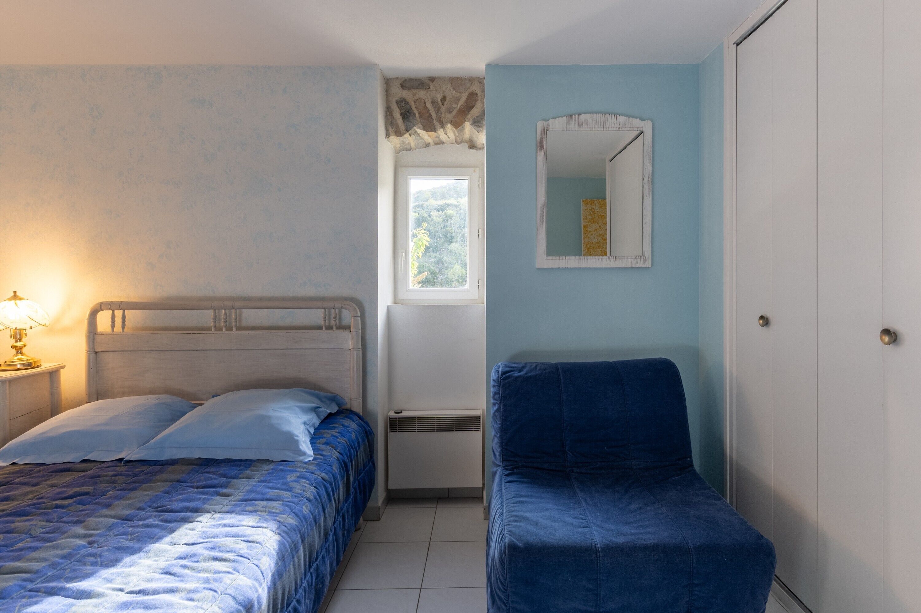 Una camera da letto con un letto, una sedia, un armadio, una finestra e uno specchio.